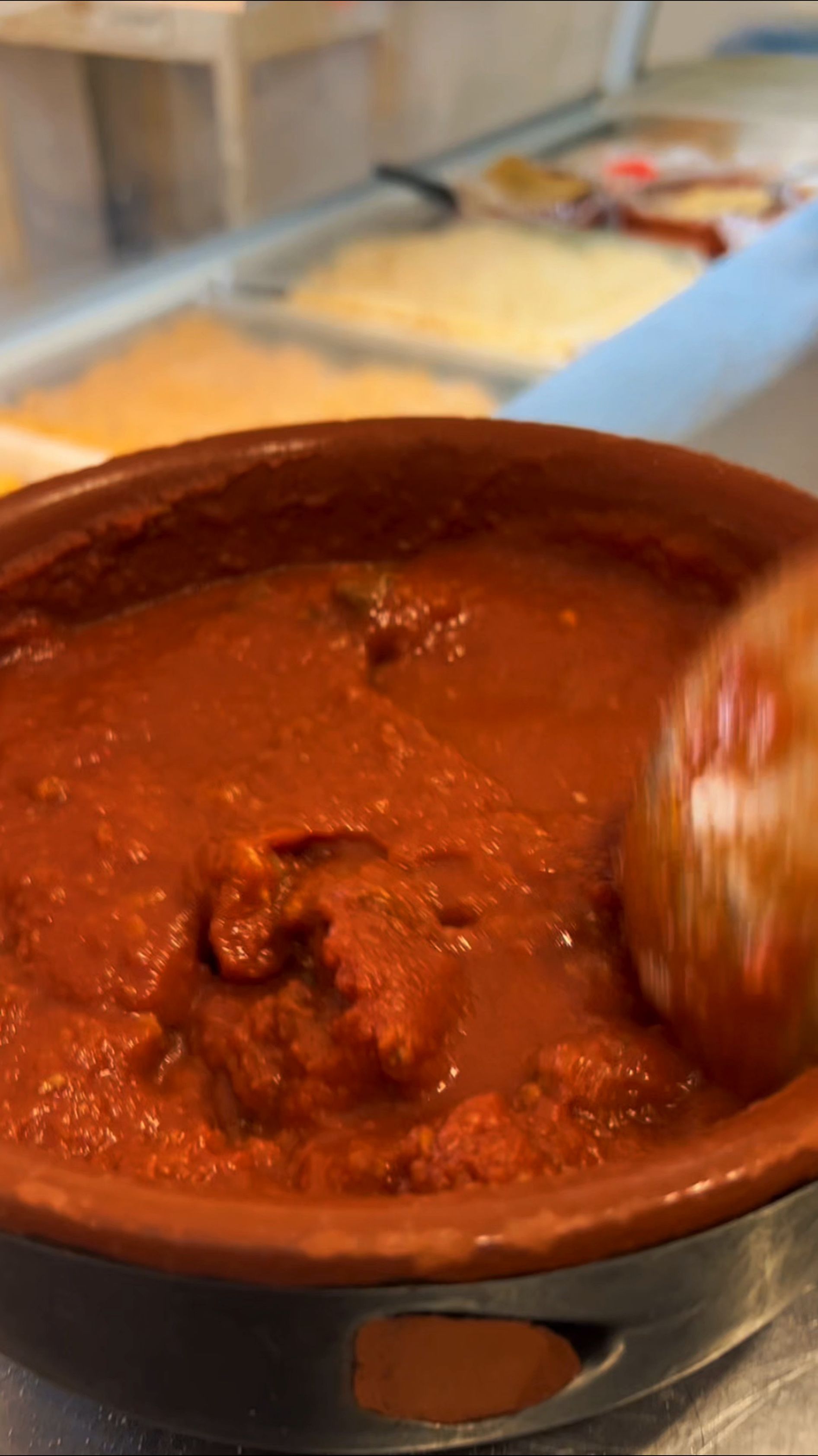 Pentola di terracotta piena di salsa rossa densa, mescolata con un cucchiaio