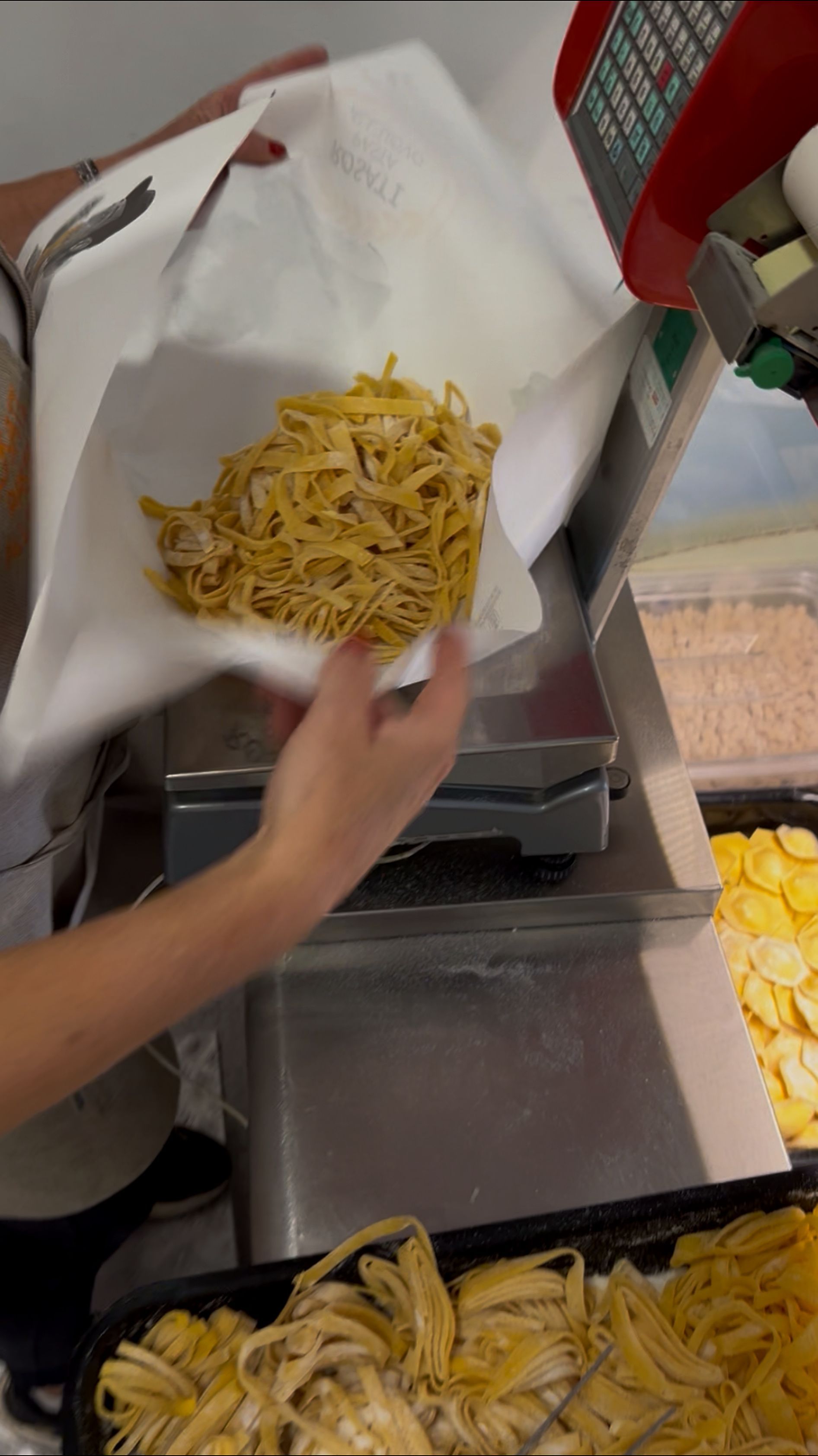 Una mano versa le patatine da un sacchetto nel cestello della friggitrice, accanto a una pila di patate affettate