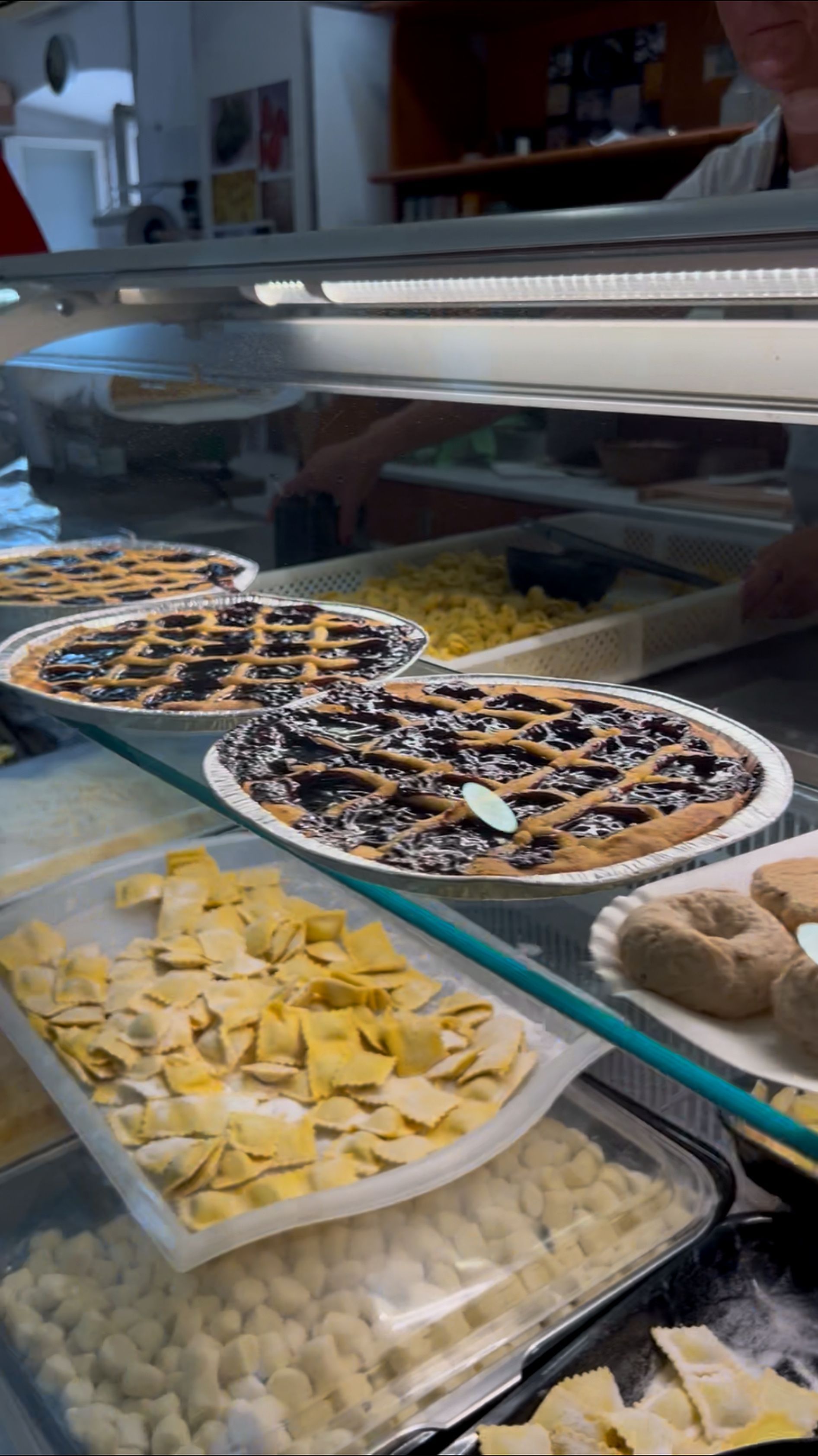 Banco dei dolci con due pizze e vassoi di pasticcini sotto una vetrina di vetro