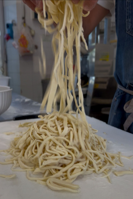 Mani che sollevano degli spaghetti per metterli su un piatto in cucina, con una montagna di pasta sotto