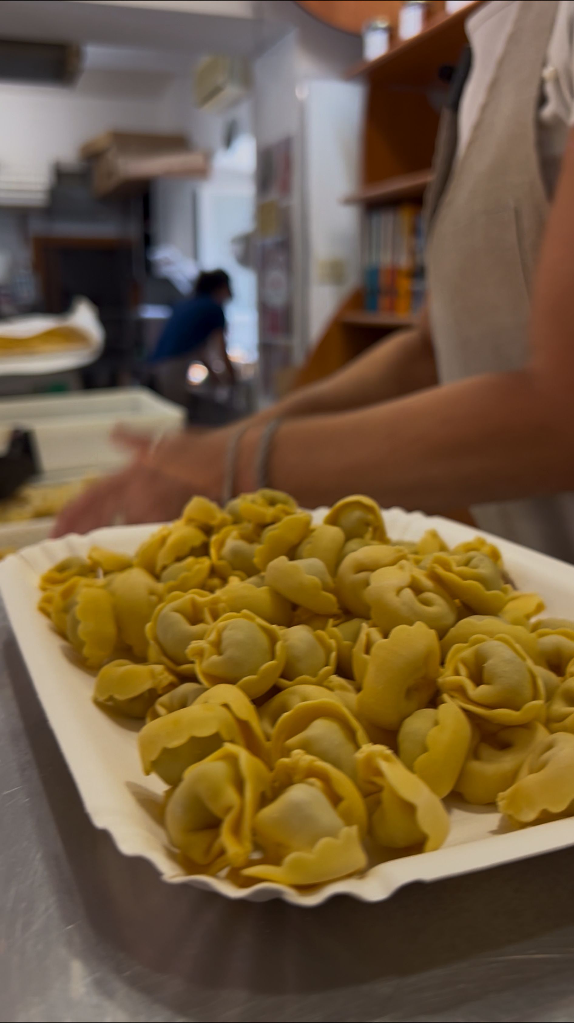 Vassoio di ravioli verdi su un tavolo, con una persona in piedi lì vicino in cucina.