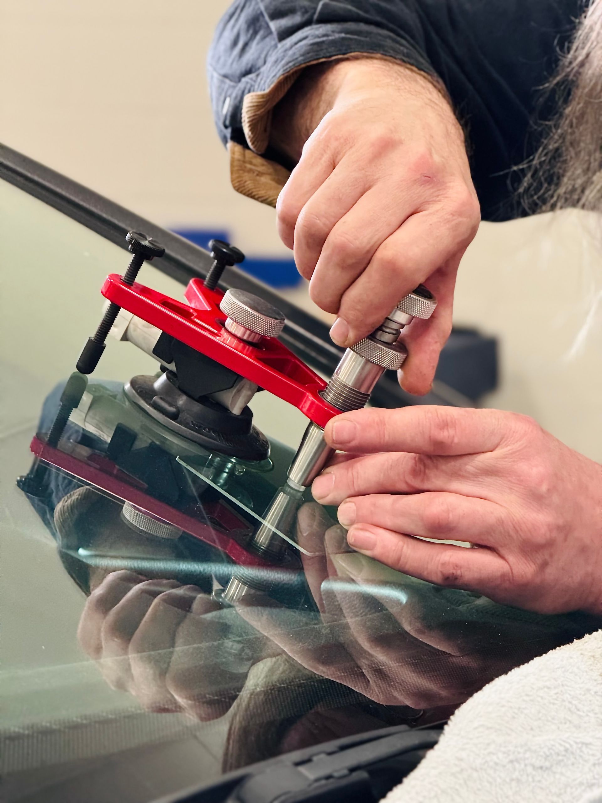 Person repairing a windshield crack with a specialized tool, close-up view.