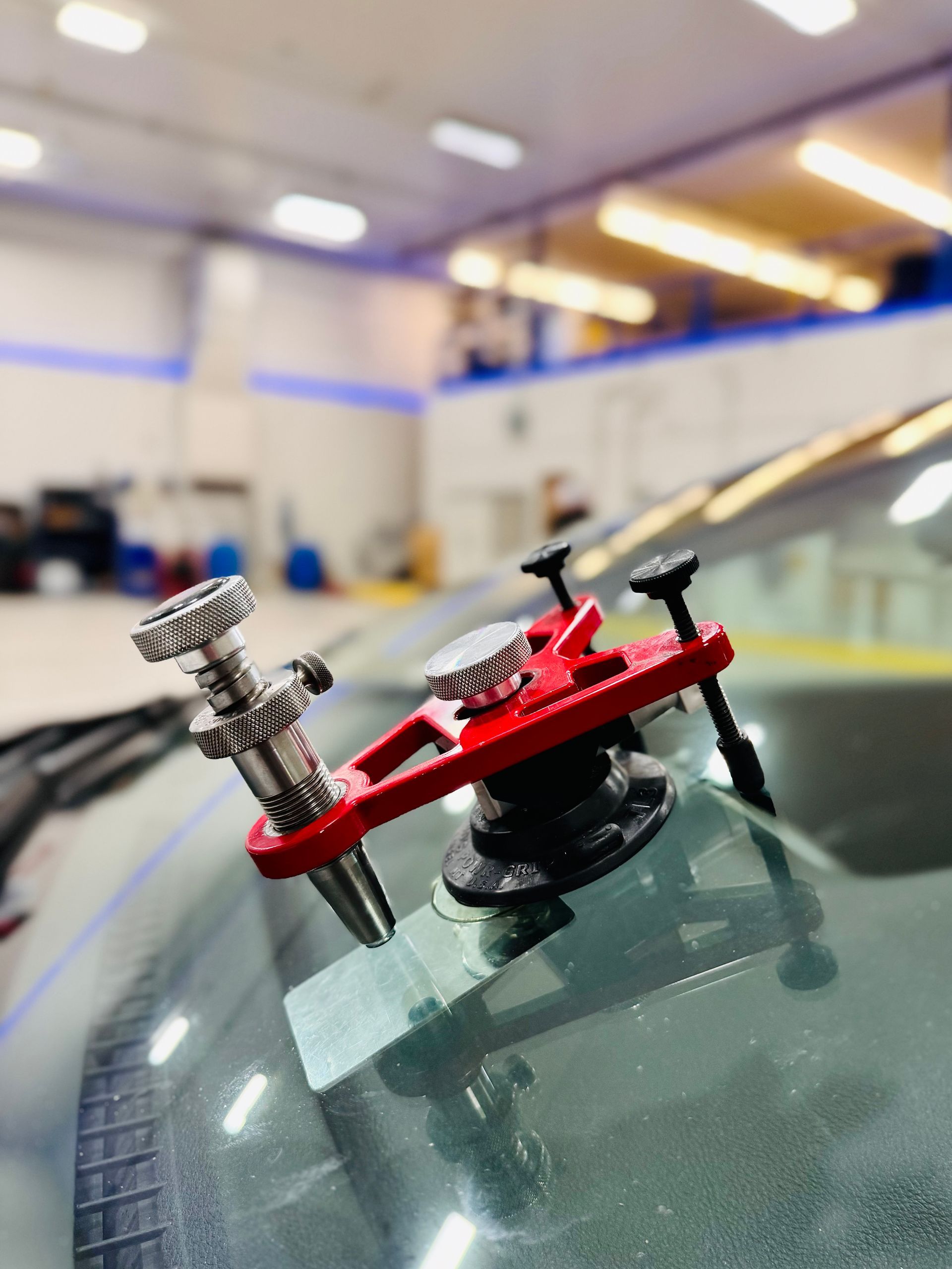 Red windshield crack repair tool on a car windshield in a repair shop.
