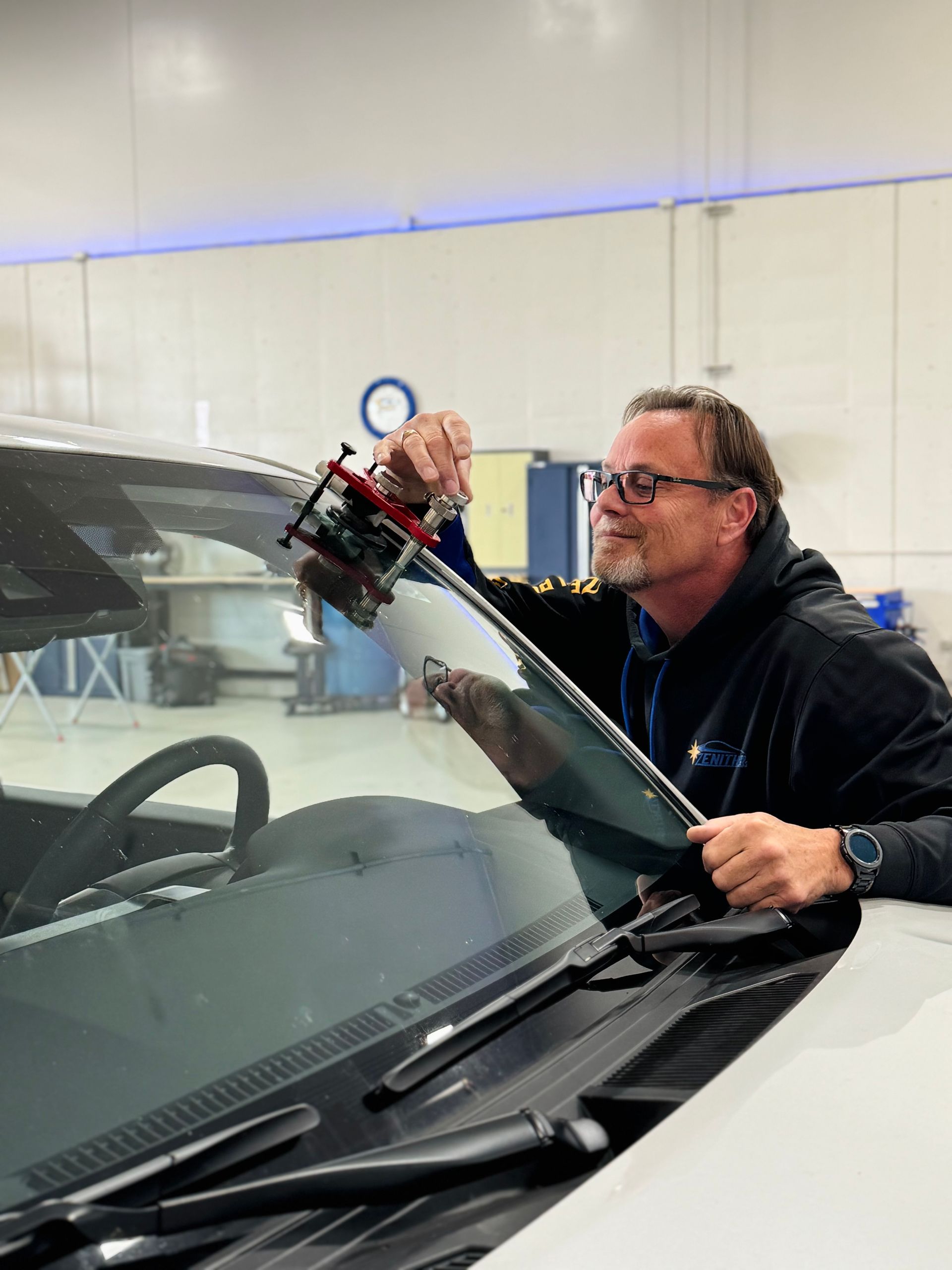 Man using a tool to repair a windshield inside a garage.