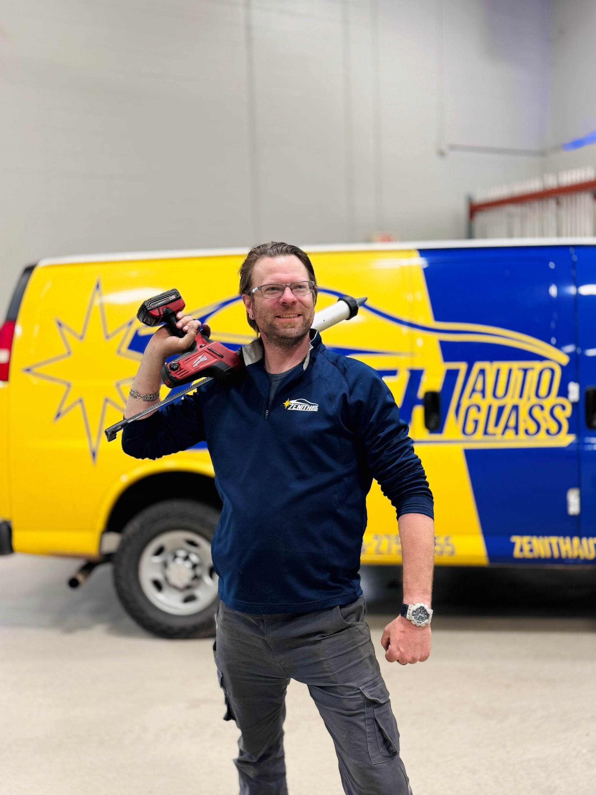 Man with a drill on shoulder stands in front of a yellow and blue van for