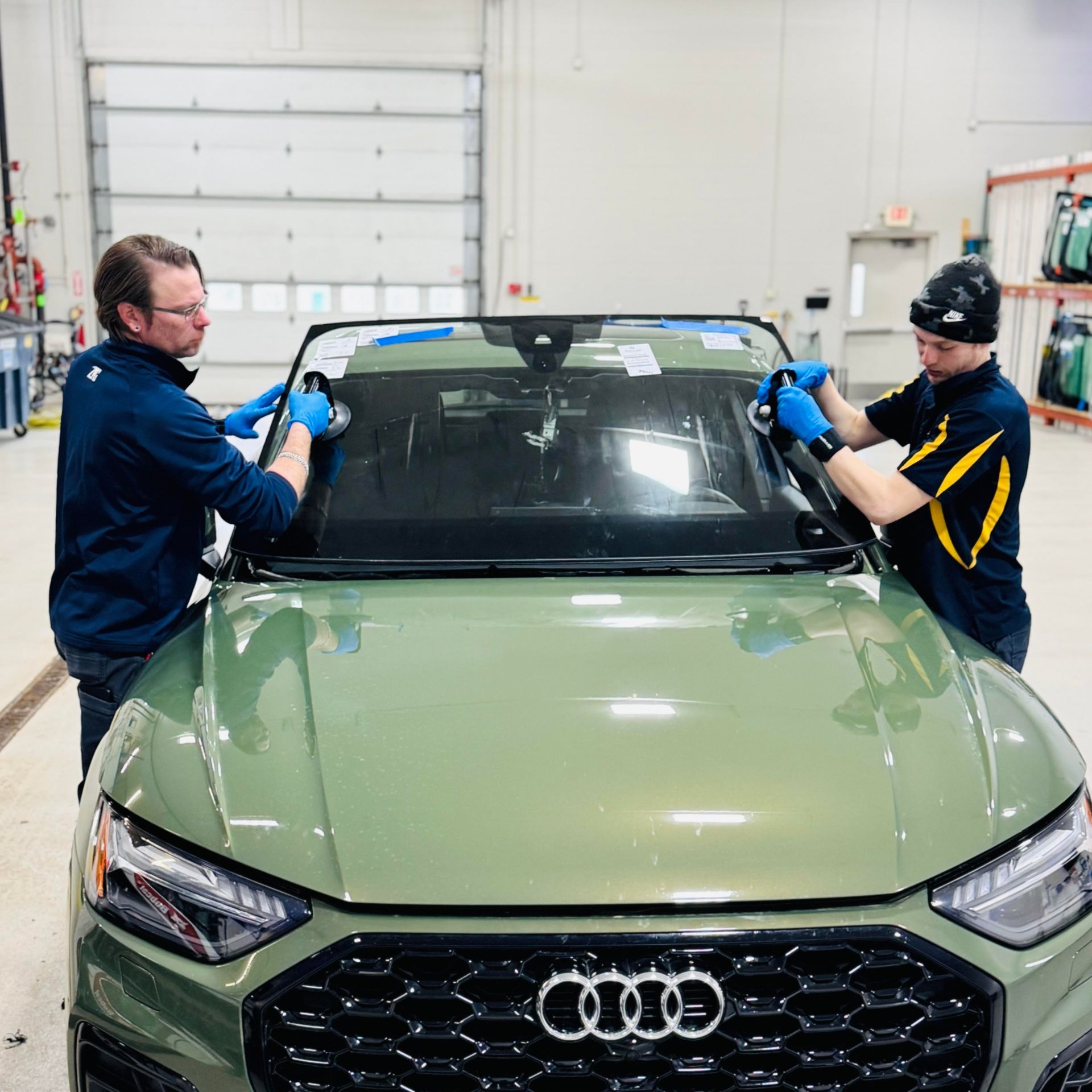 Two people installing a windshield on a green Audi. Factory setting.