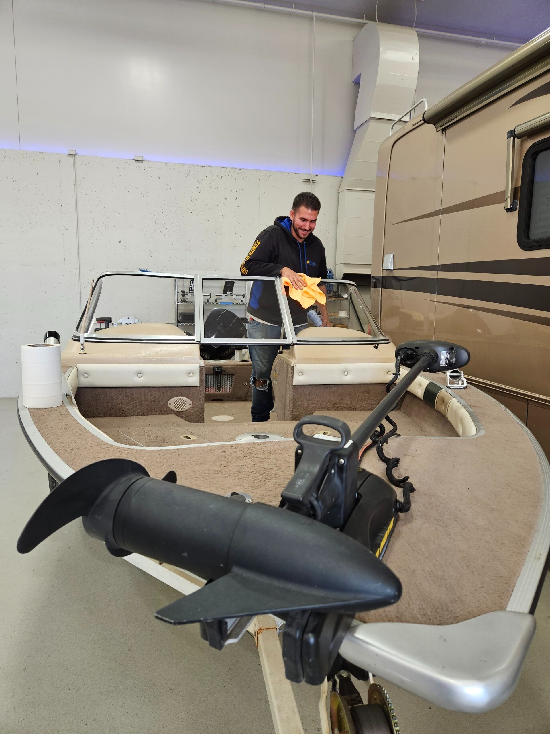 Man cleaning a boat windshield in a showroom, the boat is tan with a black propeller.