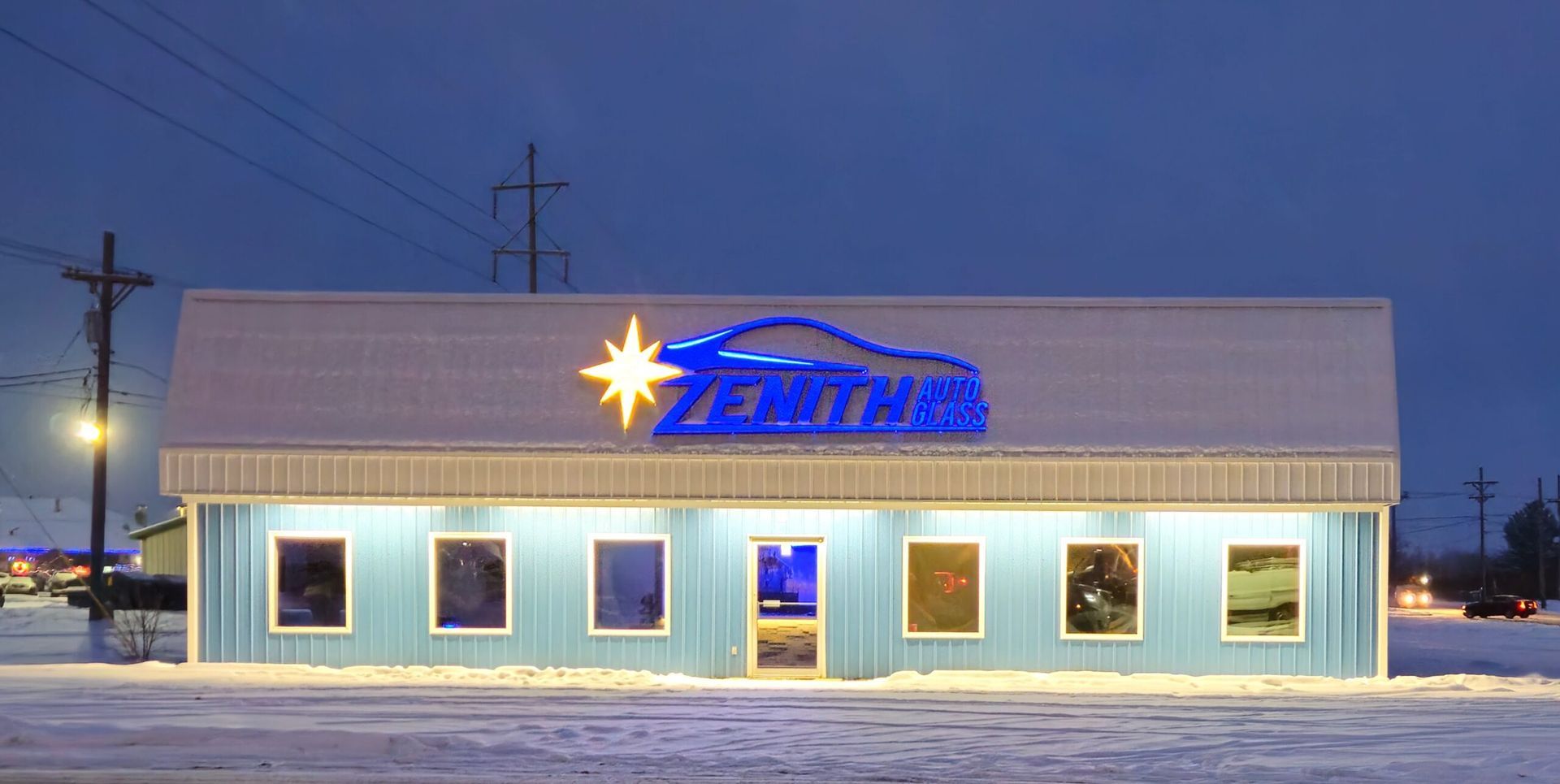 A blue building with a lighted sign and star in a snowy landscape at dusk.