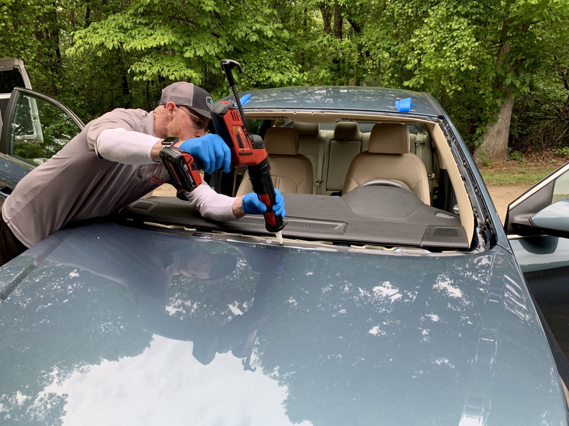 Person using a tool to remove a windshield from a blue car outdoors.