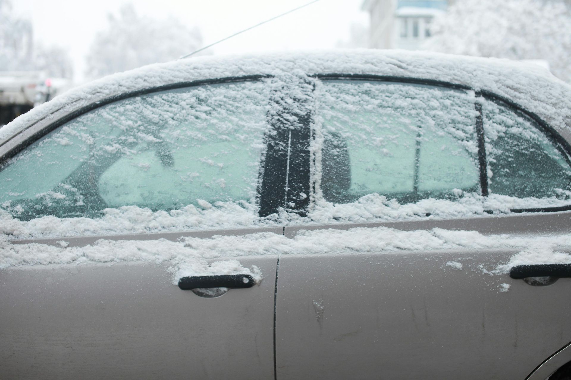 Silver car covered in snow in a snowy outdoor setting.