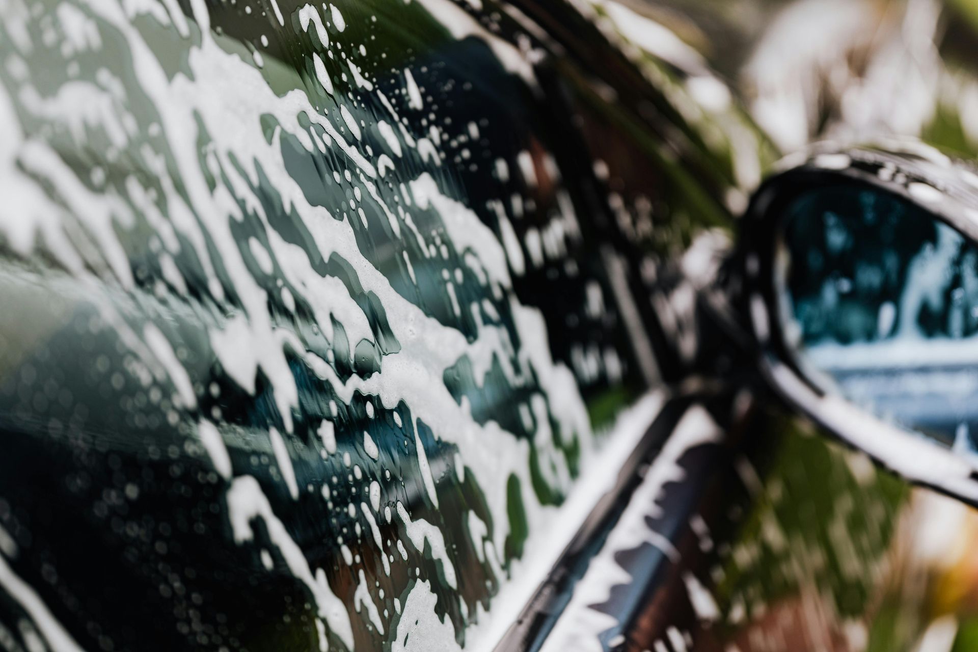 A black car covered in white soap suds, with side mirror visible.