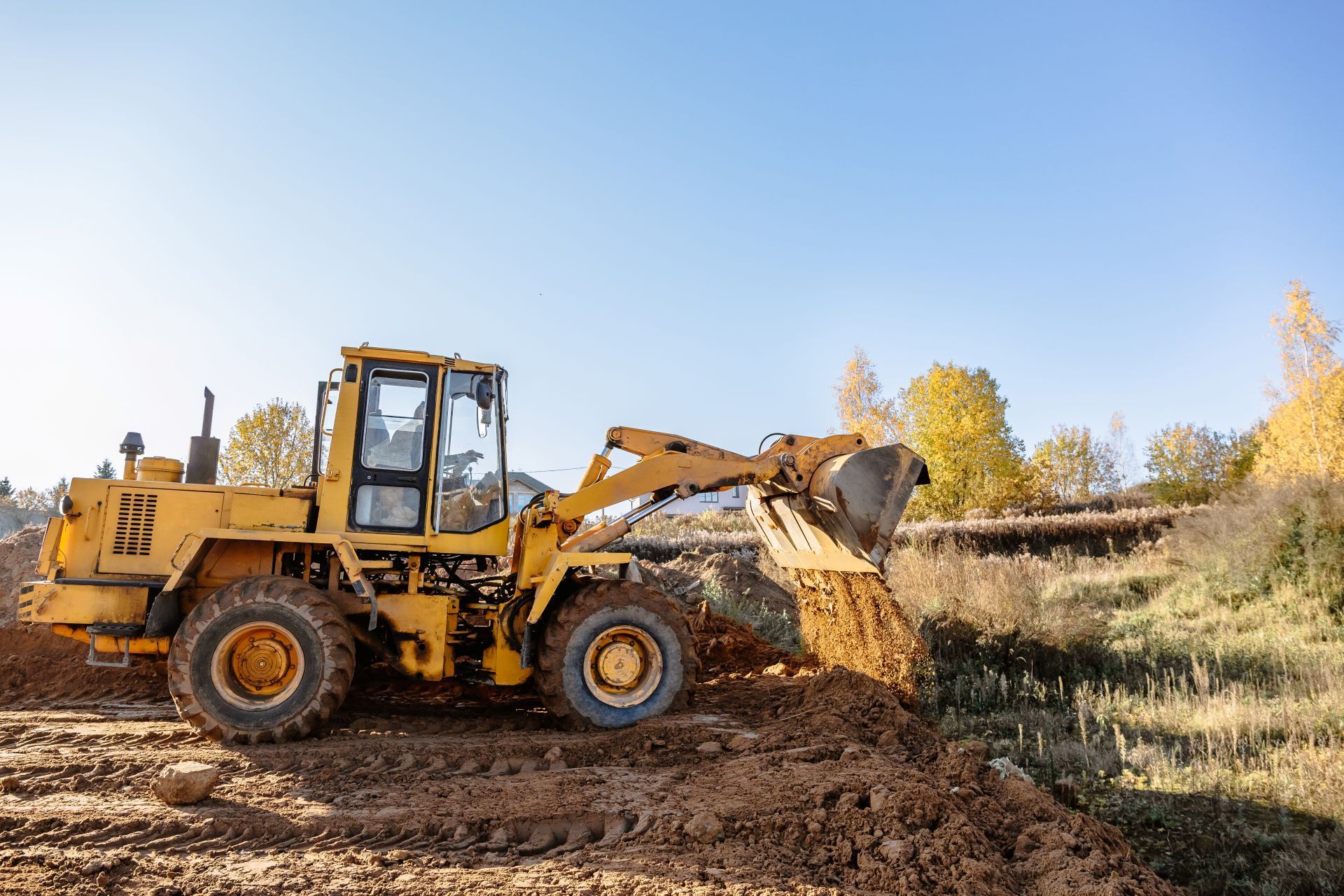 Yellow front-end loader scoops dirt on a construction site, blue sky in background.