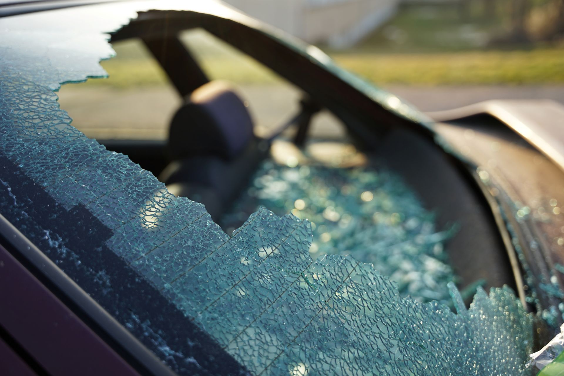 Broken car windshield, shards of glass visible, daylight setting.