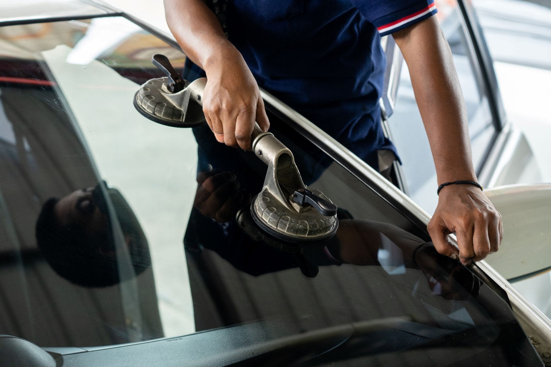 Person using suction cups to remove a car windshield in a garage.