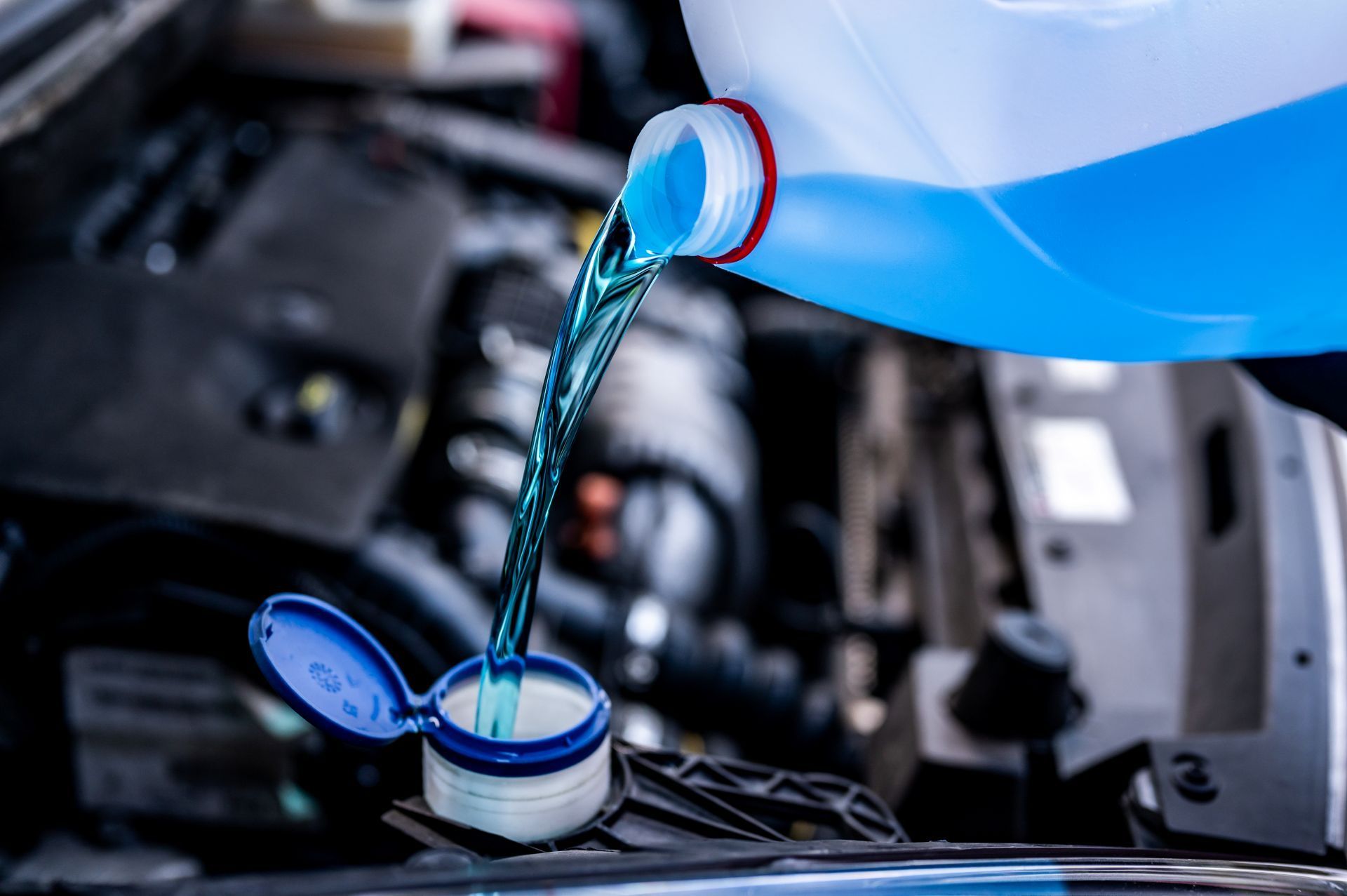 Blue windshield washer fluid being poured into a car's reservoir.