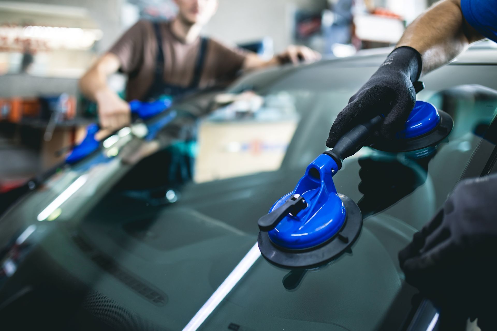 Two workers use suction cups to install a windshield in a garage.