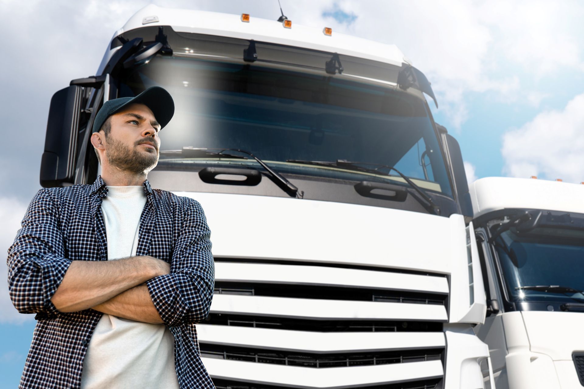 Truck driver with arms crossed, standing in front of a white semi-truck against a blue sky.