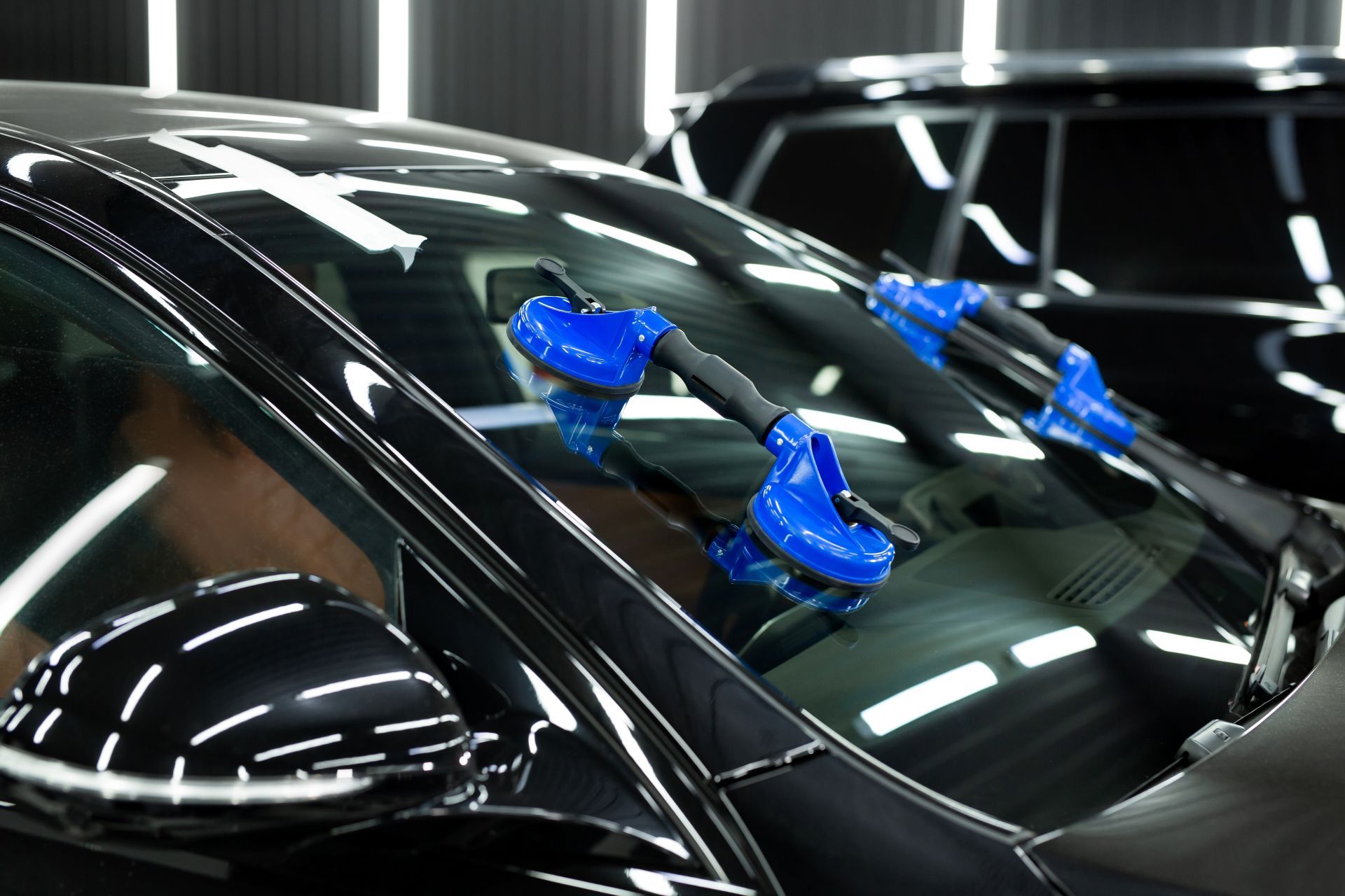 Blue suction cups on a black car windshield in a well-lit auto shop, reflecting bright overhead lights.