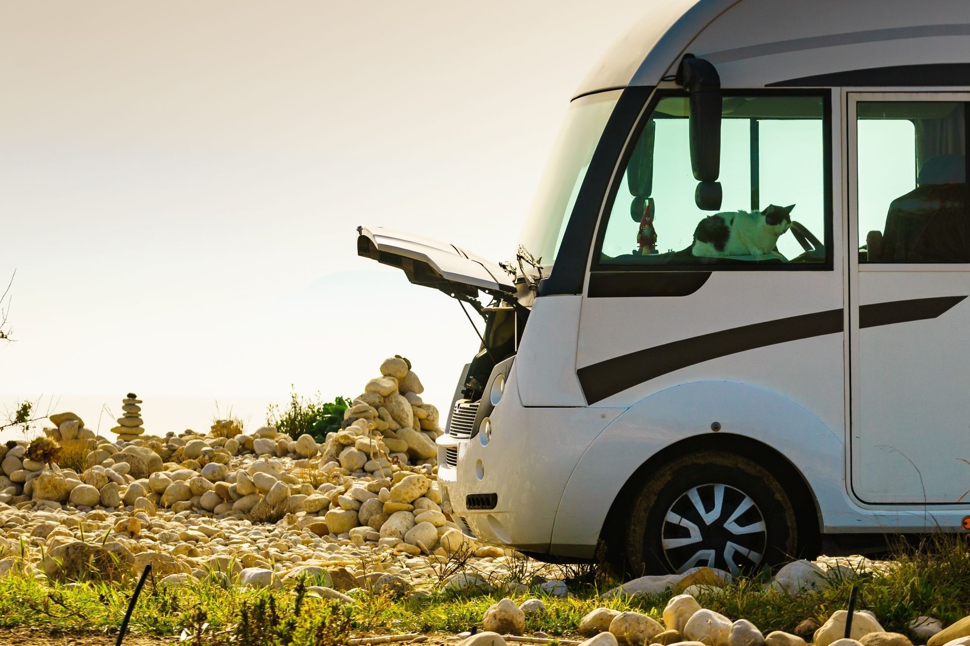 White RV parked on a rocky beach, hood open.
