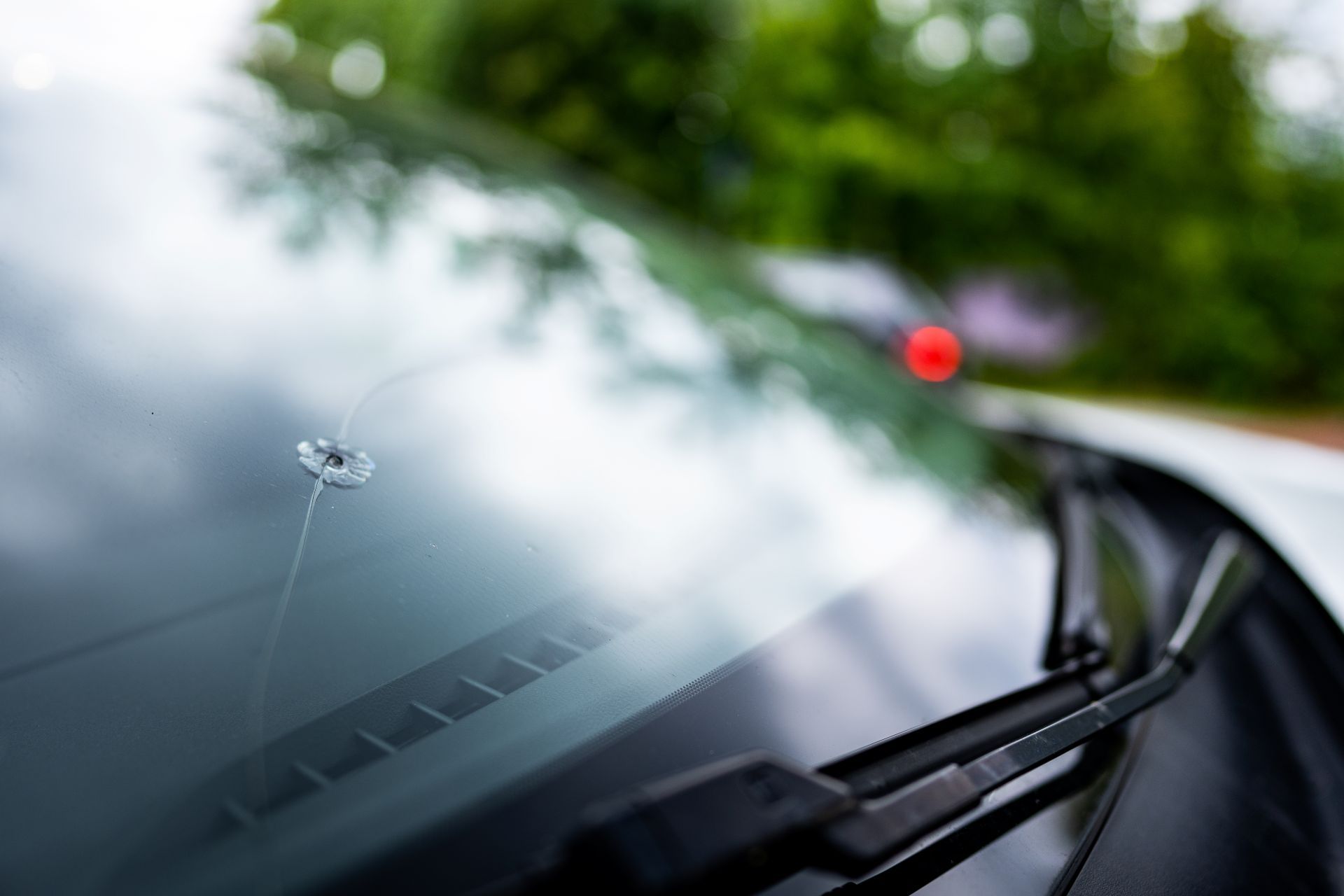 Windshield with a crack in it; a car in a blurred outdoor setting.