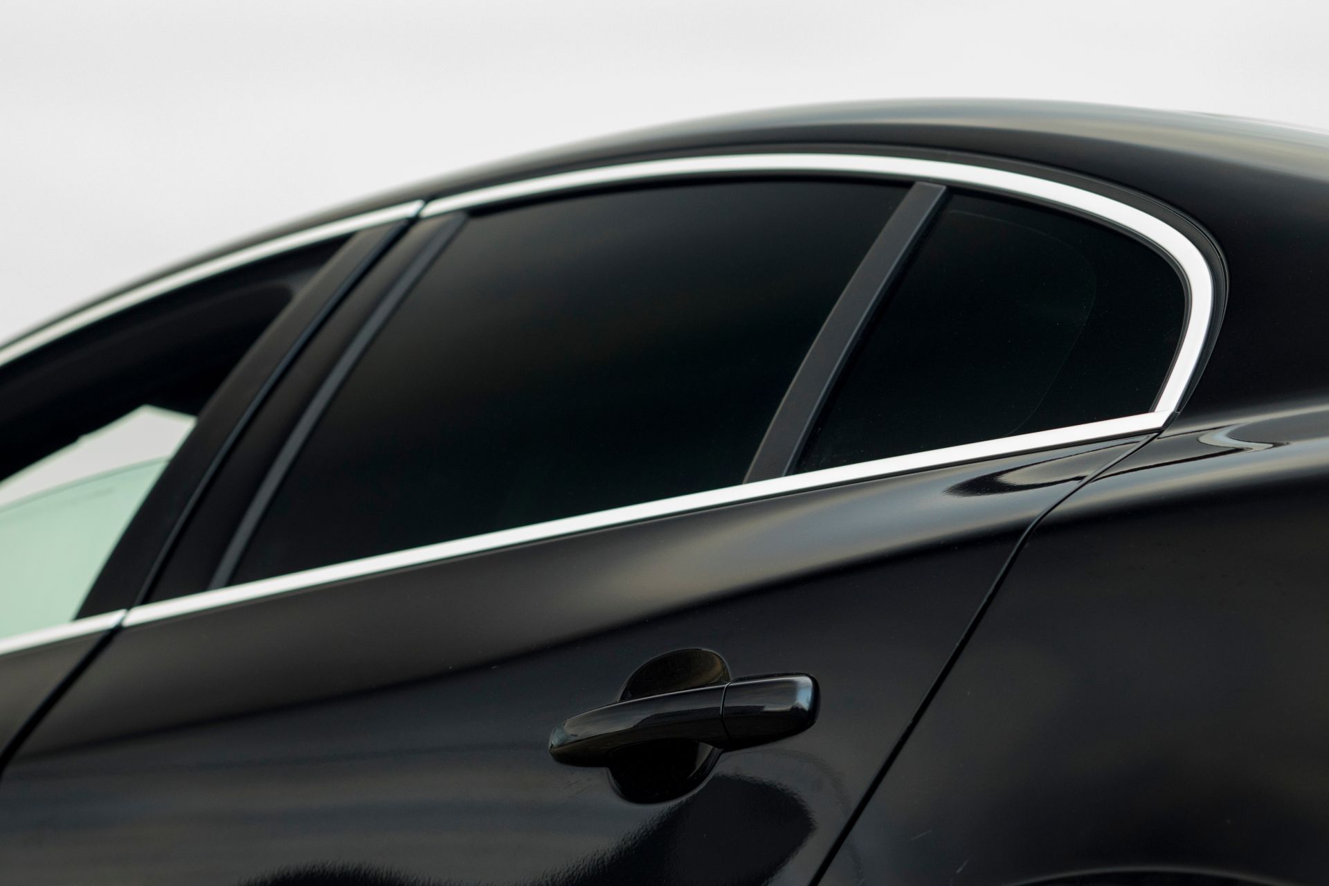 Black car's side with tinted windows, chrome trim, and door handle against a white backdrop.