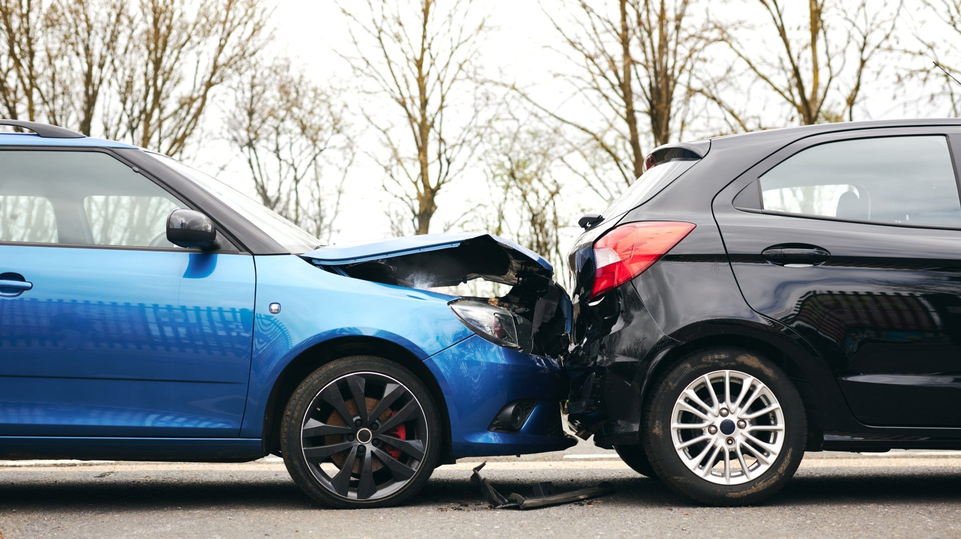 Two cars, blue and black, in a rear-end collision on a road, both damaged.