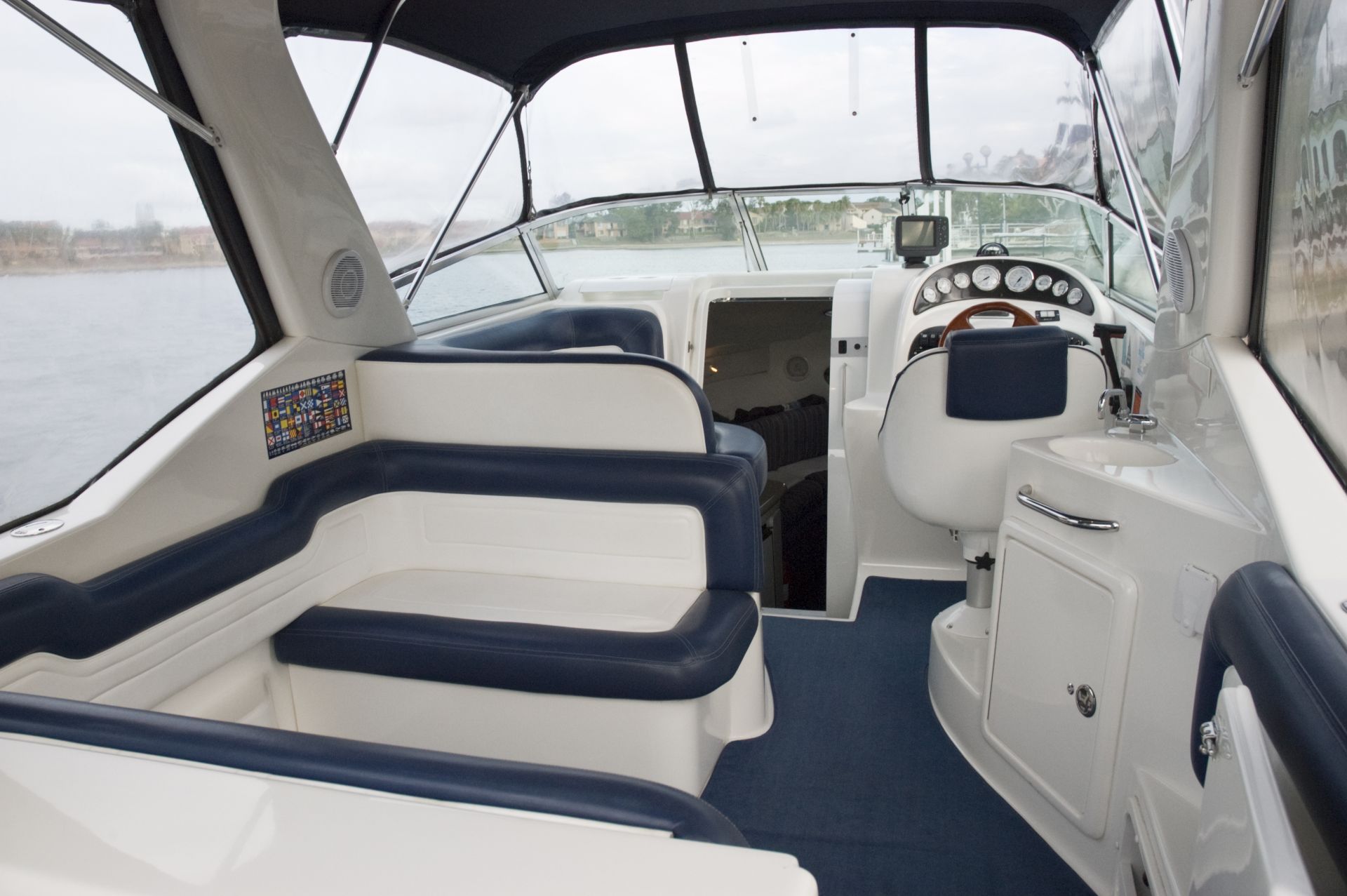 Interior of a boat with white and navy blue seats, helm station, and windows, on a body of water.