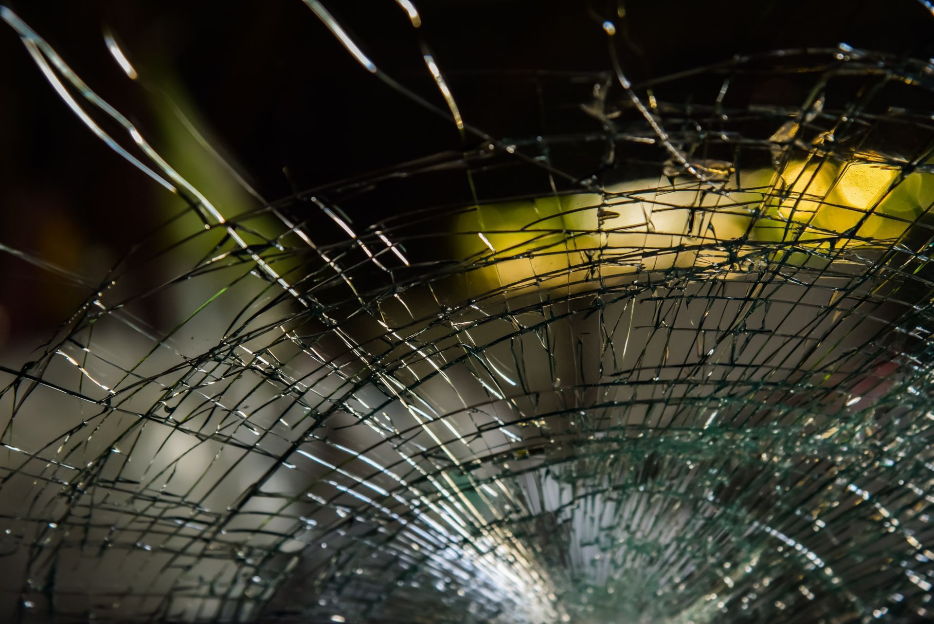 Shattered windshield, radiating cracks. Blurred background of green and yellow suggests outdoors.