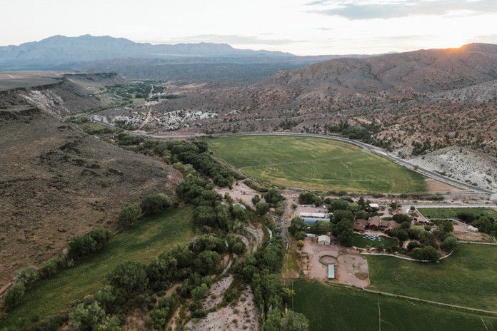 Aerial view of a green valley with fields, a winding river, and rocky mountains at sunset