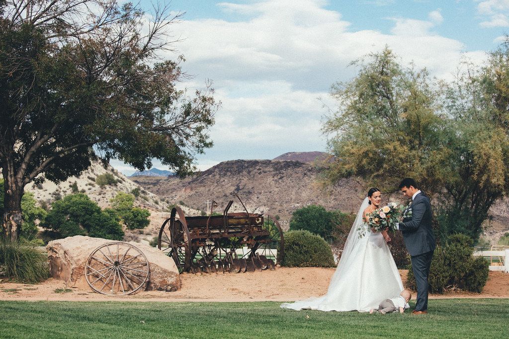 Bride and groom stand outdoors near a rustic wagon in a scenic garden setting