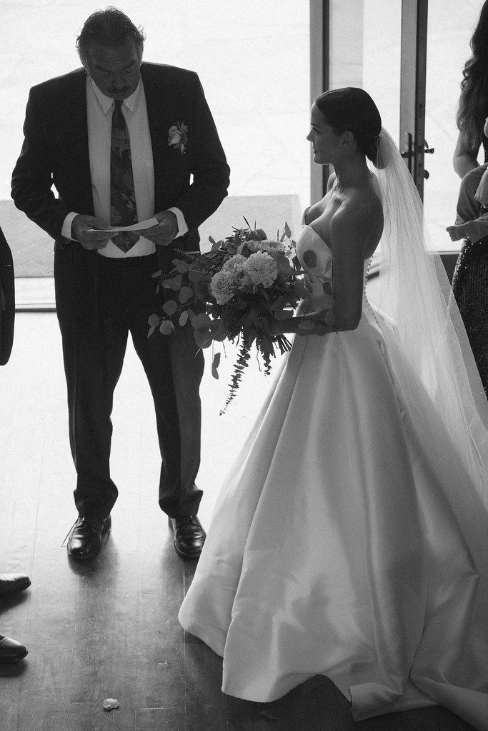 Bride and groom stand together during a wedding ceremony, the bride holding a bouquet.