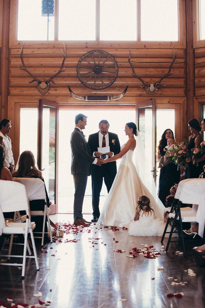 Wedding ceremony in a barn, bride and groom standing before officiant as guests watch under rustic beams