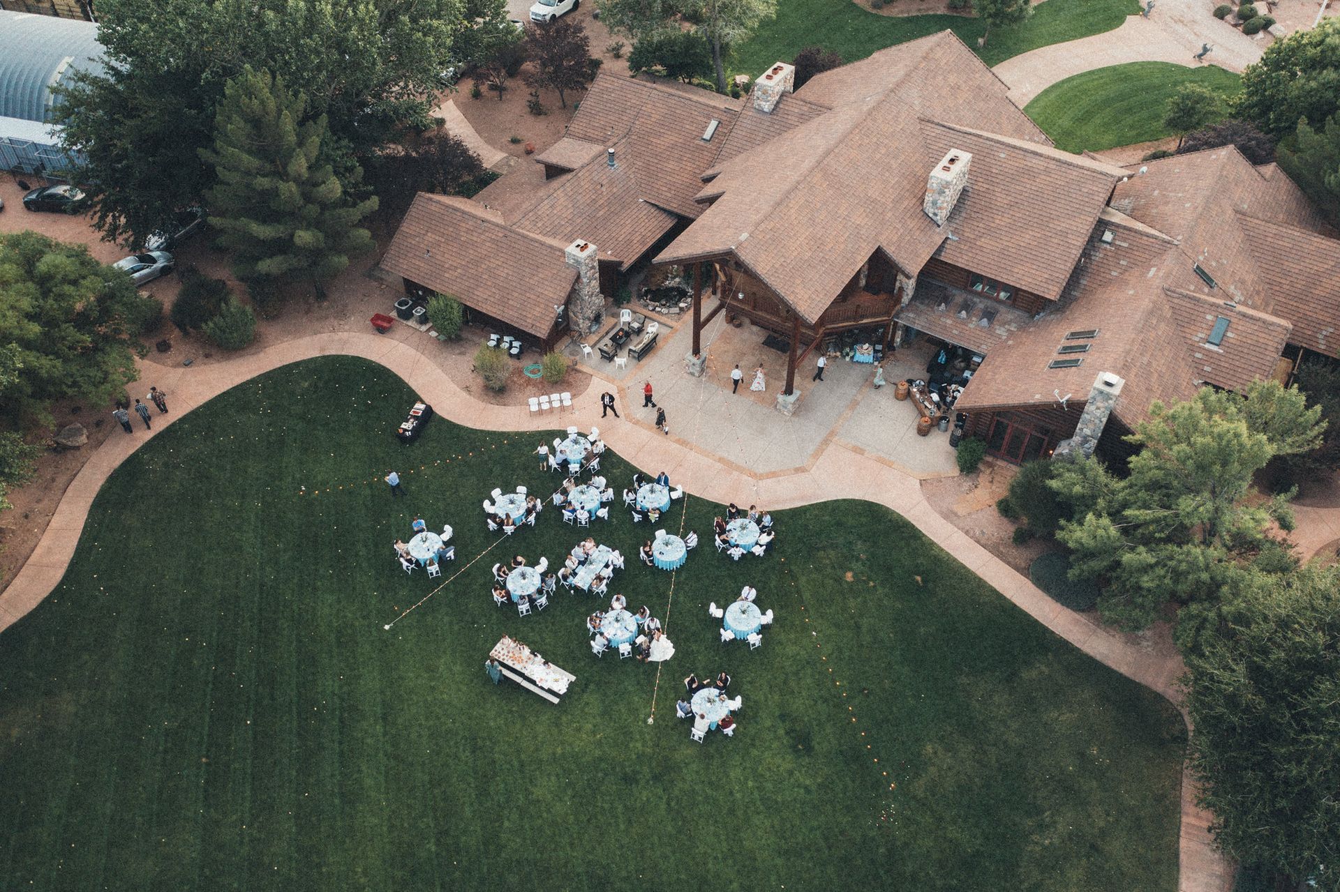 Aerial view of a rustic lodge and lawn with white tables and chairs set for an outdoor event