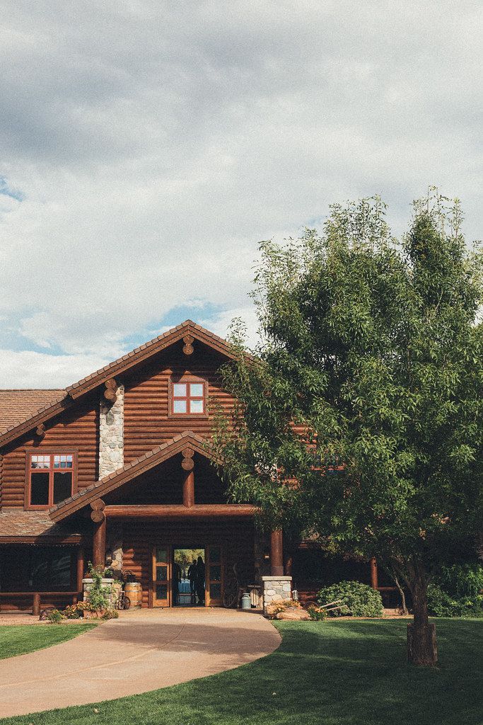 Rustic lodge entrance with a wooden porch and a tree in front under a cloudy sky
