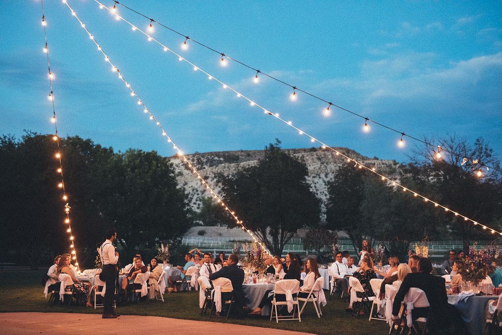 Outdoor evening gathering under string lights with seated guests at tables and a mountain backdrop