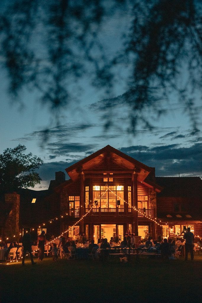 Lit lodge glowing at dusk, with guests gathered outside under a dark blue sky.