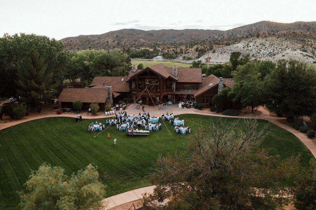 Outdoor gathering on a grassy lawn in front of a lodge, with hills in the background.