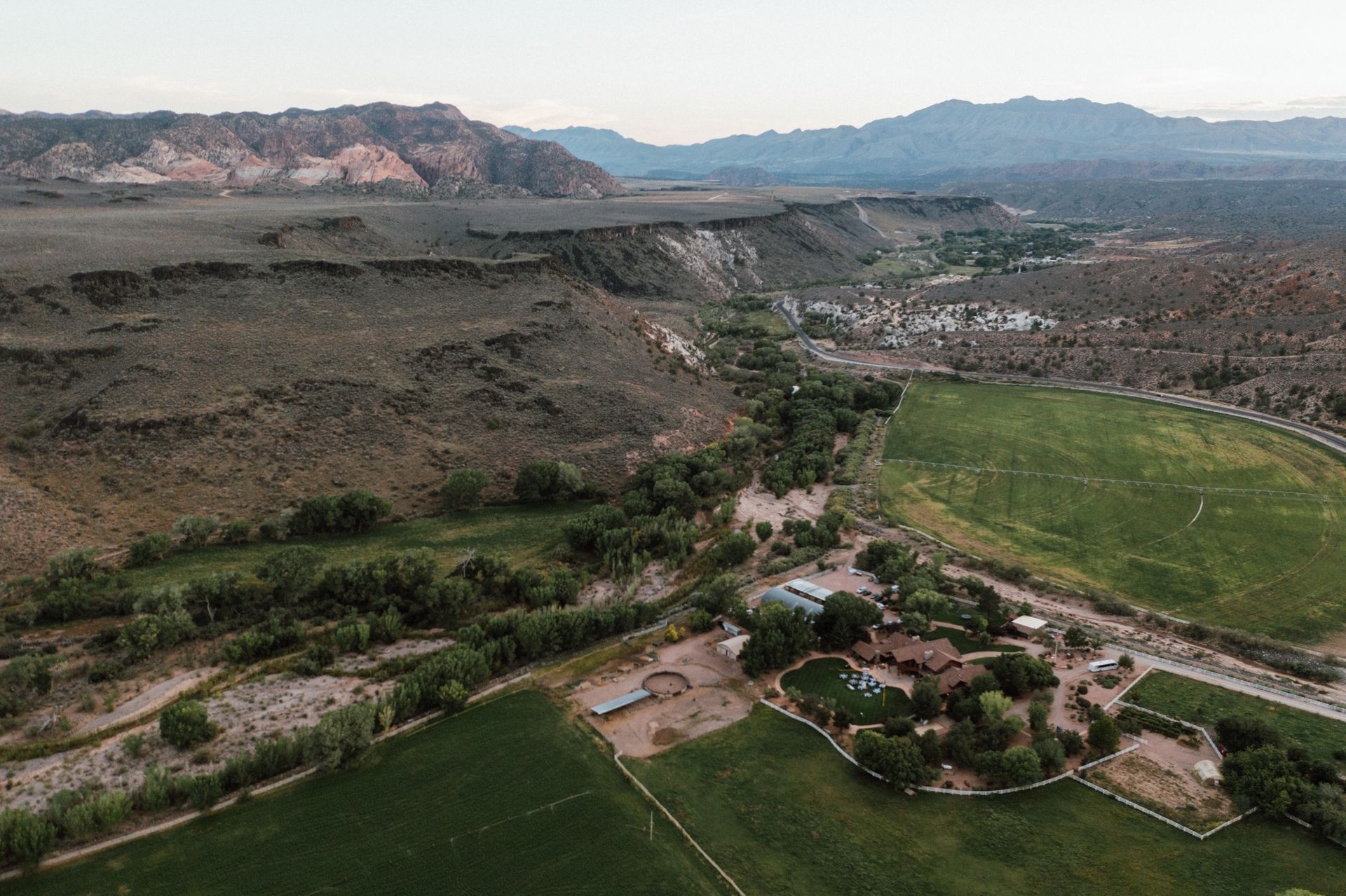 Aerial view of a green valley with a river, small buildings, and rugged mountains in the distance