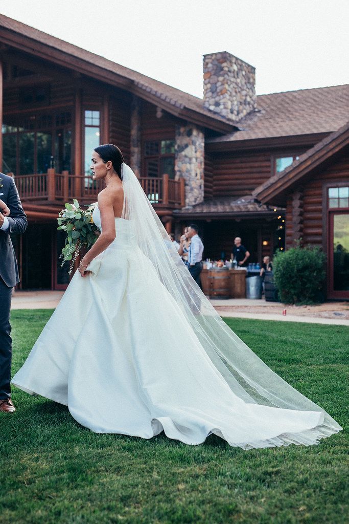 Bride in a white wedding gown walking on grass outside a rustic log building