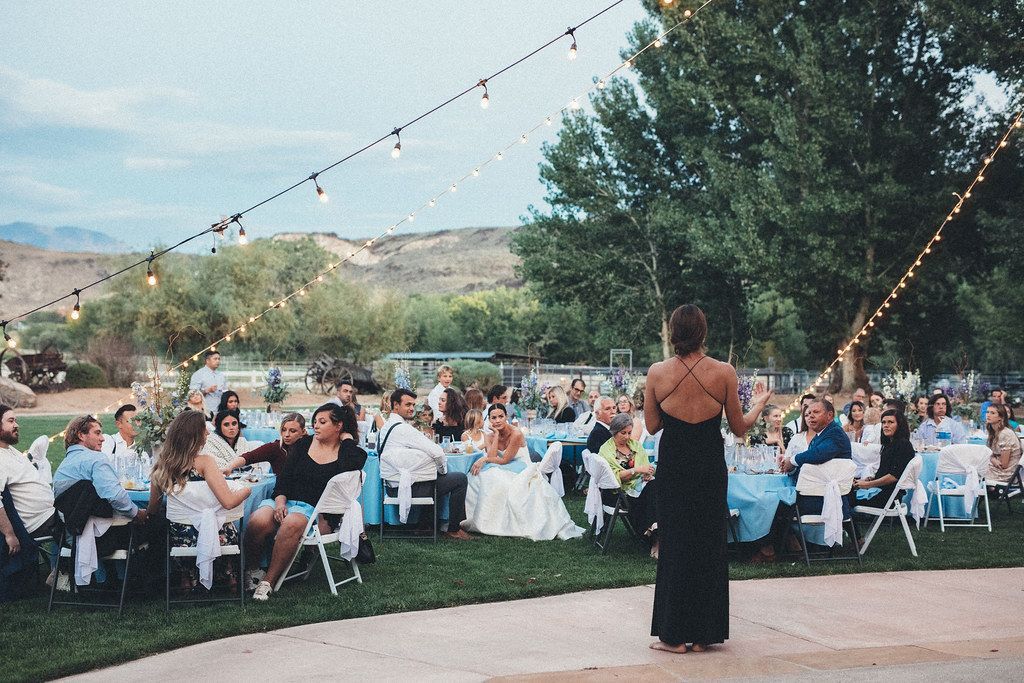 Outdoor wedding reception with guests seated at tables and a woman in a black dress standing in the foreground