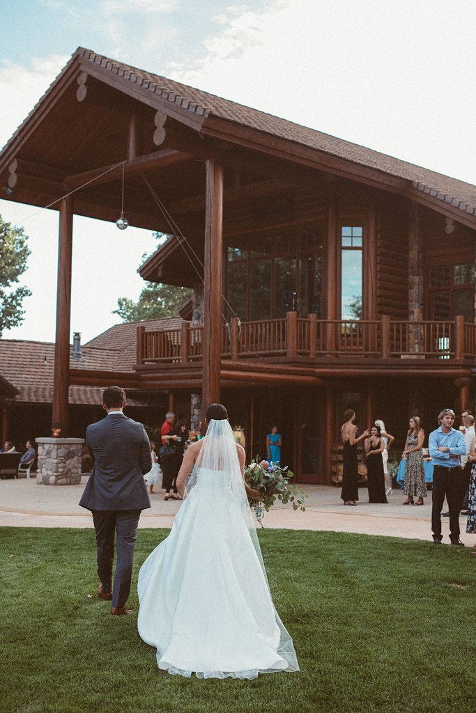 Bride and groom walking toward a rustic wooden lodge during an outdoor wedding ceremony
