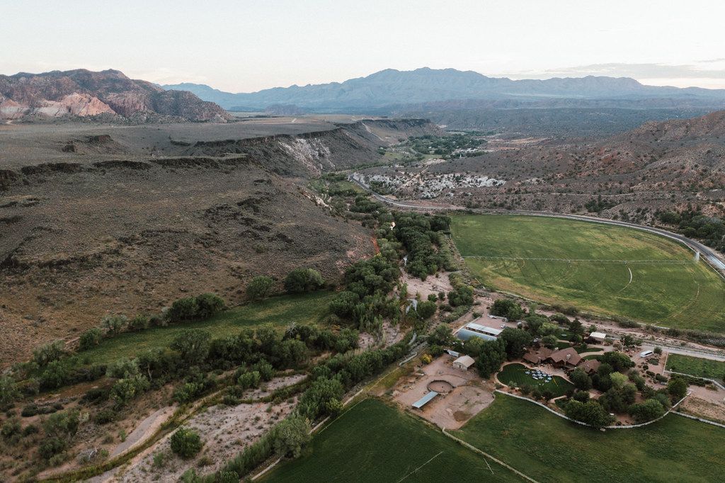 Aerial view of a valley with green fields, rocky hills, and a small village under a hazy sky
