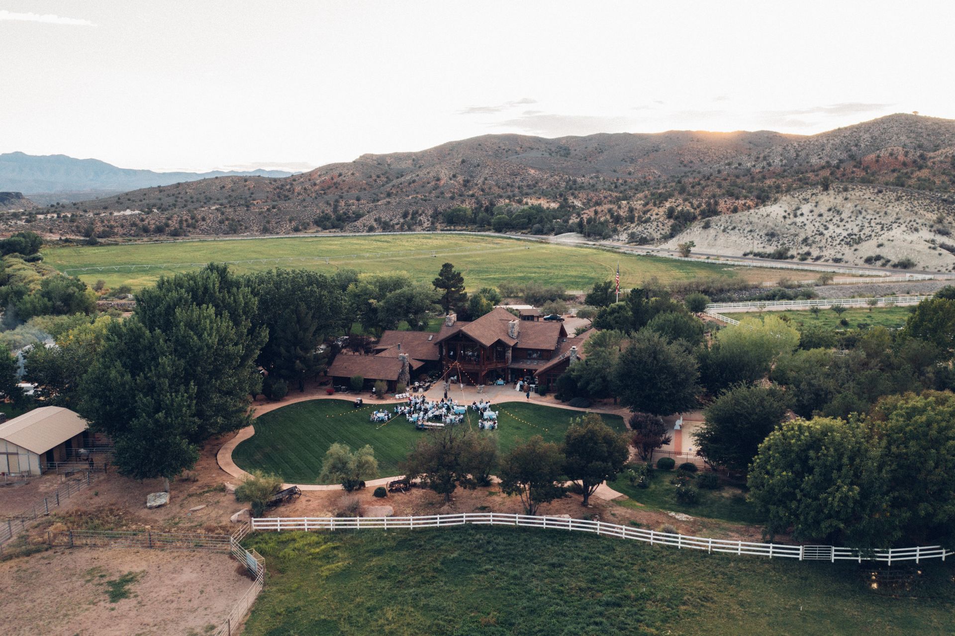 Aerial view of a lodge with pool and garden amid green fields and rocky hills