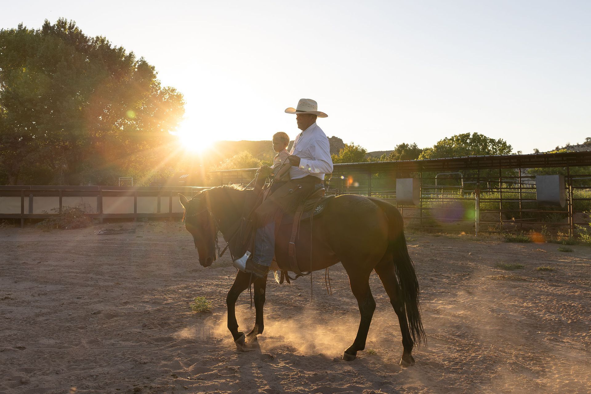 Two people standing with a horse in a grassy field at sunset, one holding a hat.