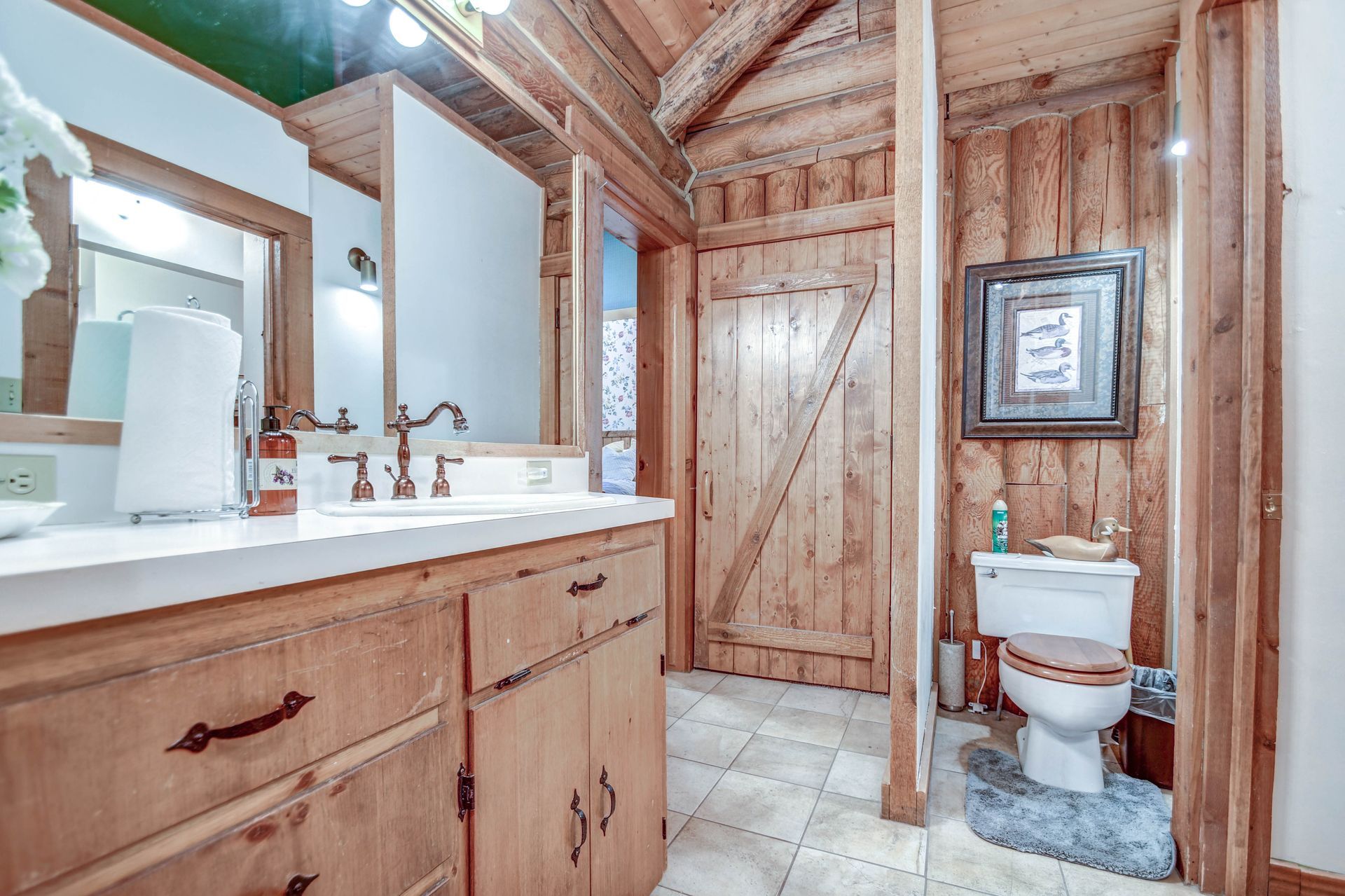 Rustic bathroom with wood-paneled walls, vanity sink, mirror, and toilet under a framed picture.