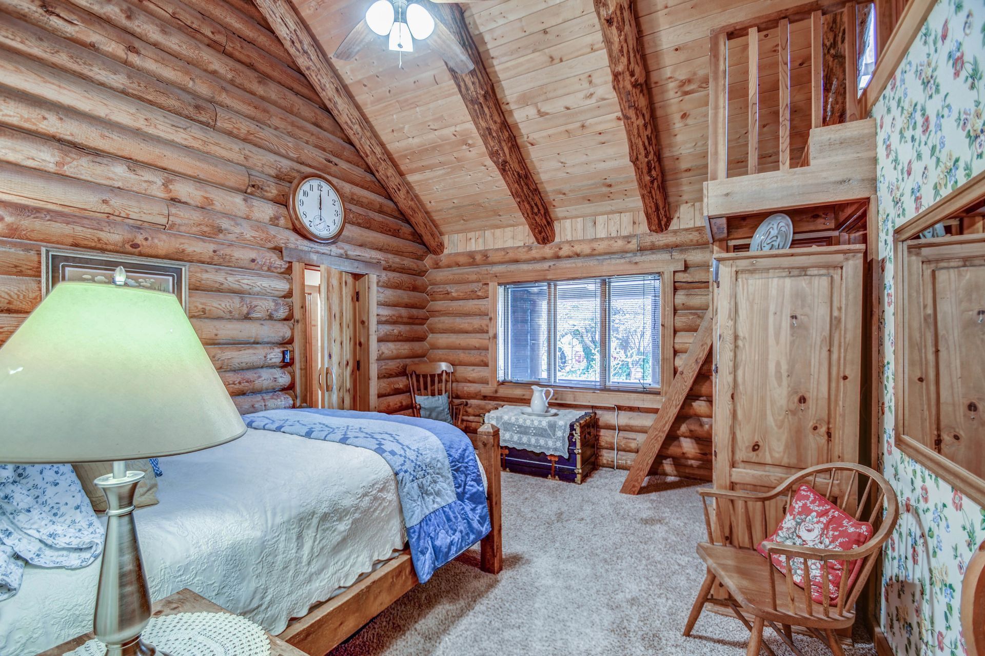 Rustic log cabin bedroom with a bed, wooden ceiling beams, dresser, and window seat