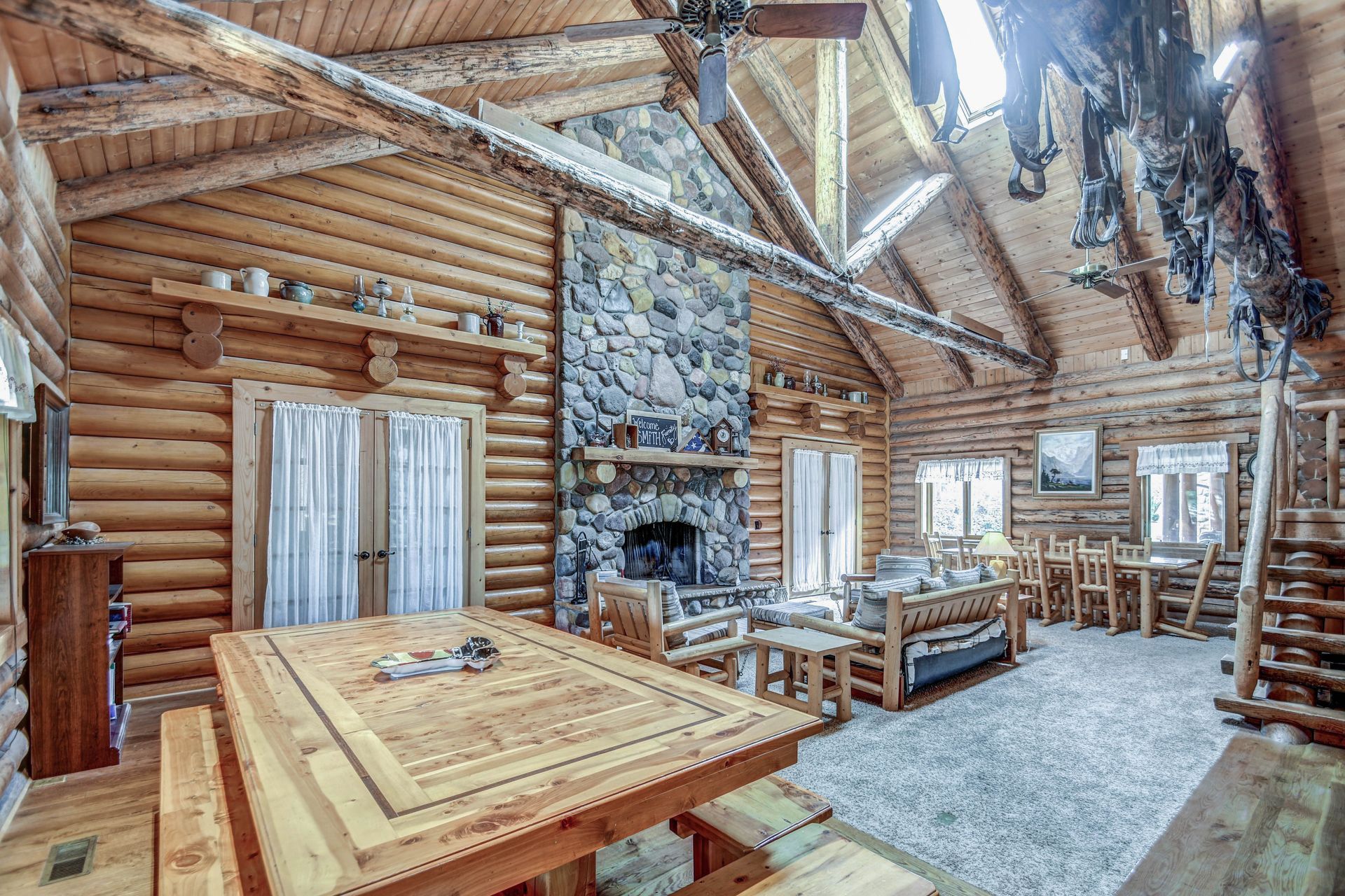 Rustic log cabin living room with stone fireplace, wood beams, and dining table