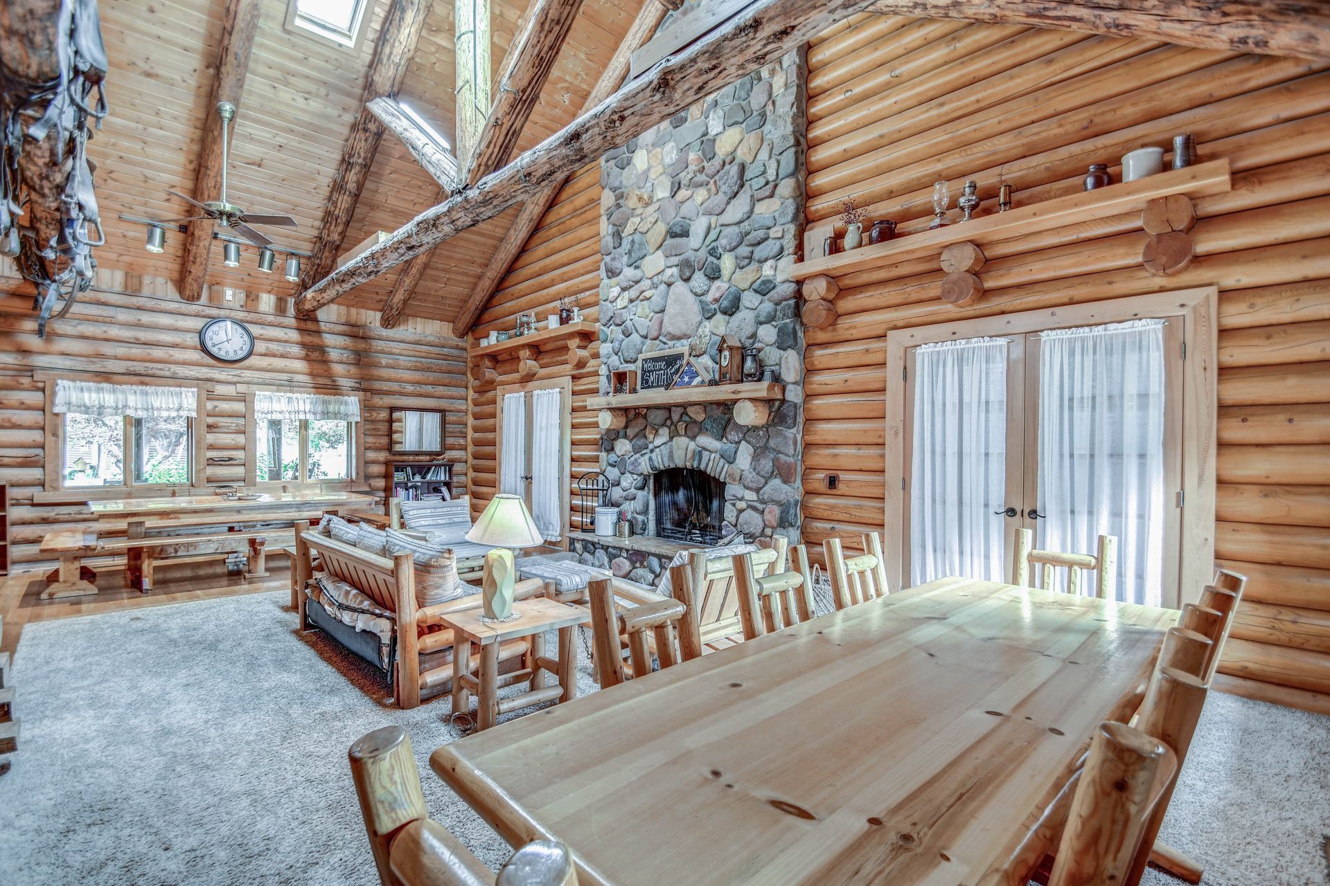 Rustic log cabin dining room with wooden table, stone fireplace, and large windows