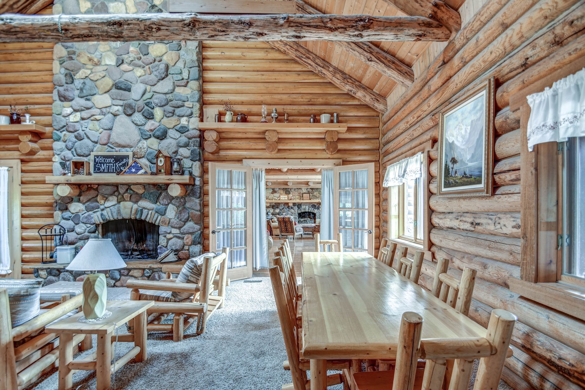 Rustic log cabin dining room with stone fireplace, long wooden table, and large windows