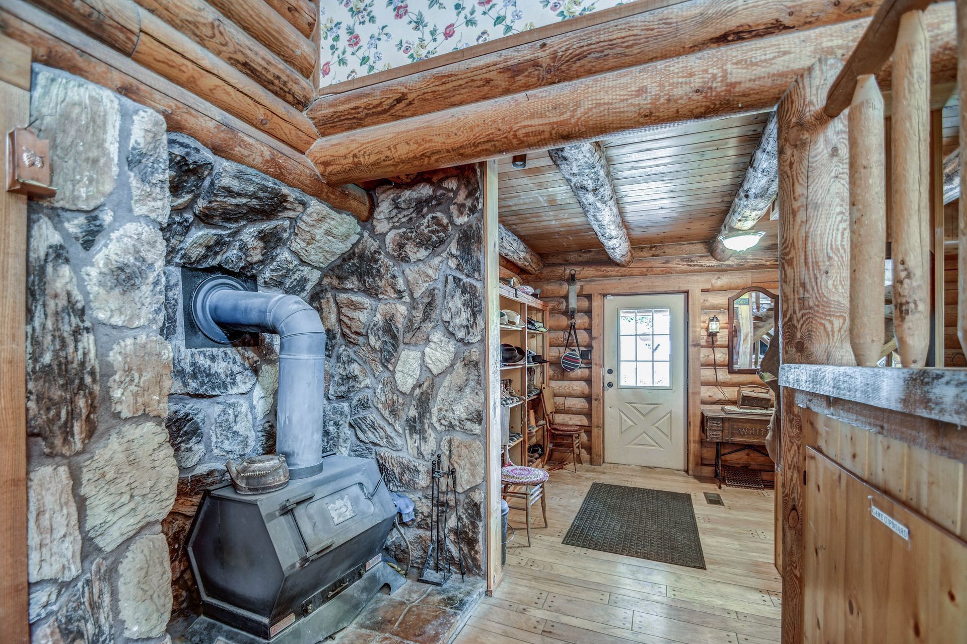 Rustic cabin interior with a wood stove, log walls, and a hallway leading to a door